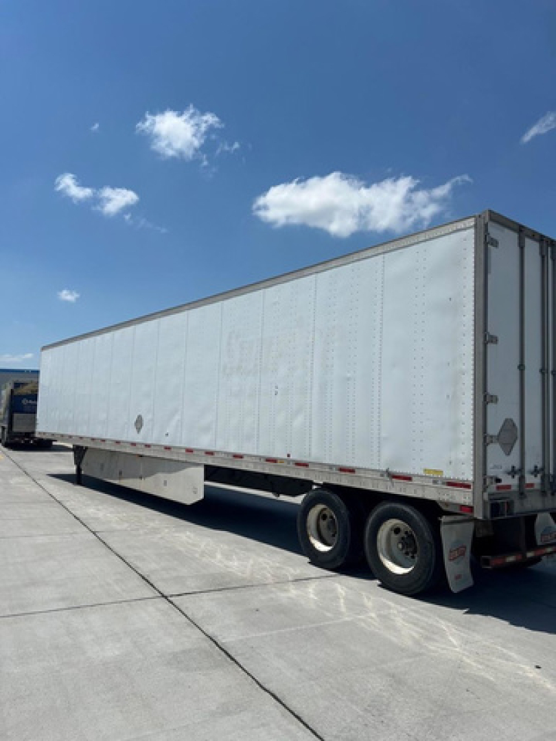 Trailer van showing side of a long white utility trailer with three axles and tandem wheels.