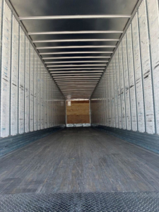 Interior of a utility van trailer showing long empty cargo space with metal side walls and a wooden bulkhead at far end.