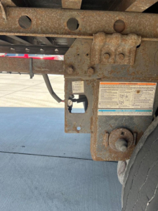Trailer hitch and frame with rusted components, label stickers, and wiring near wheel on a utility van trailer.