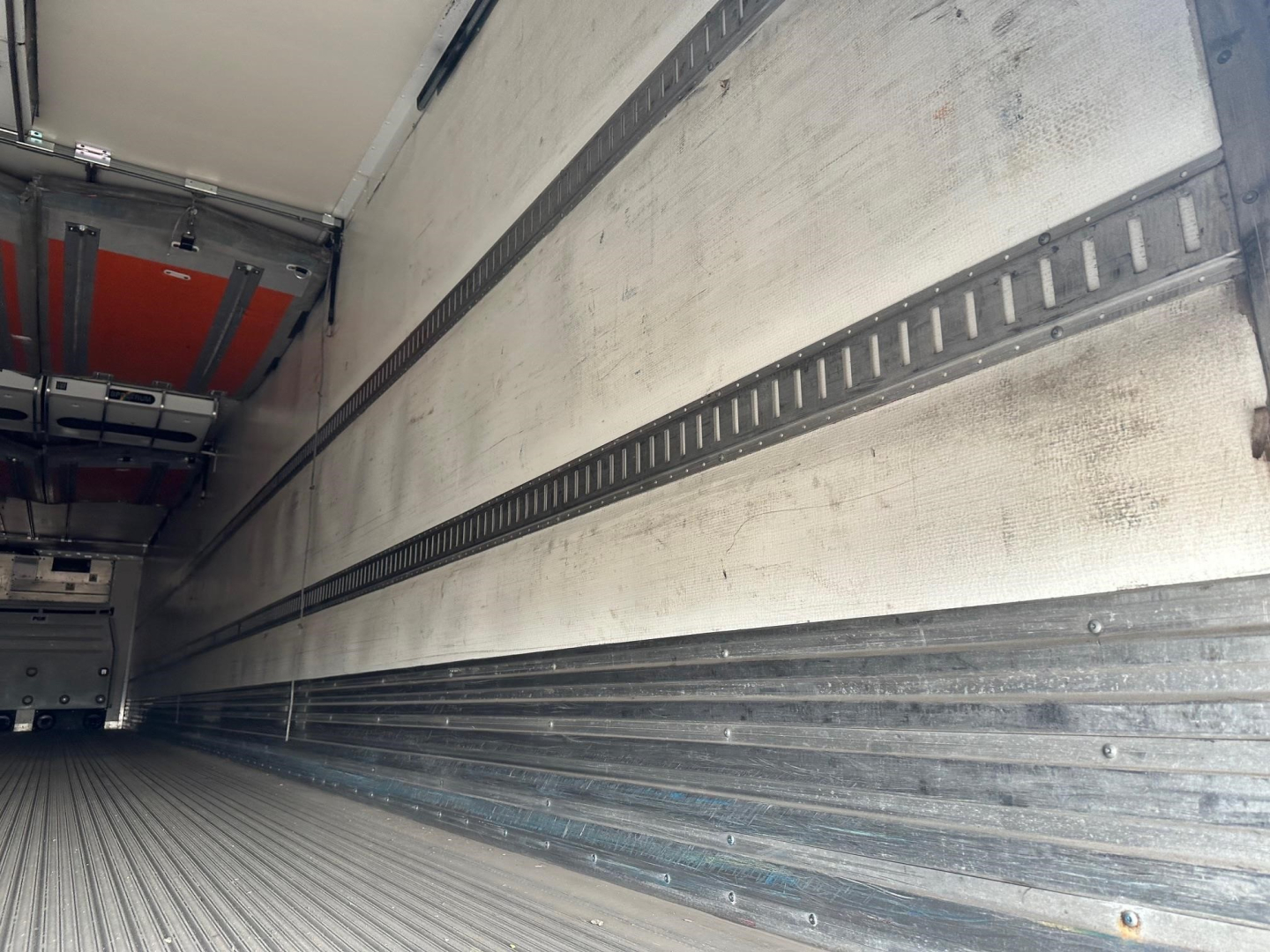 Reefer trailer interior with metal cargo walls and E-track rails, empty floor, side walls show fitted refrigeration lining.