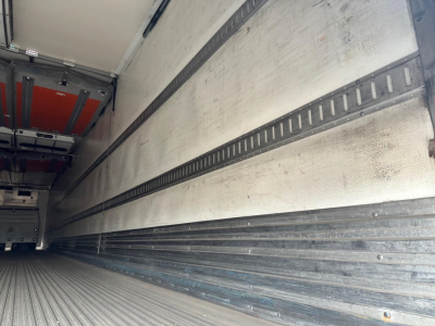 Reefer trailer interior with metal cargo walls and E-track rails, empty floor, side walls show fitted refrigeration lining.