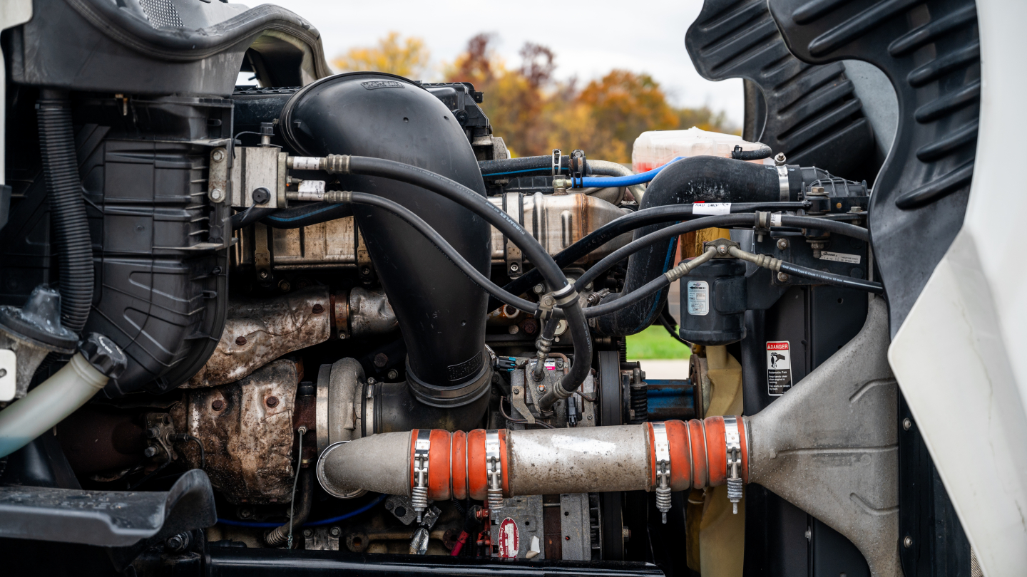 Engine bay of Freightliner Cascadia showing hoses, radiator, and exhaust components with orange clamps.