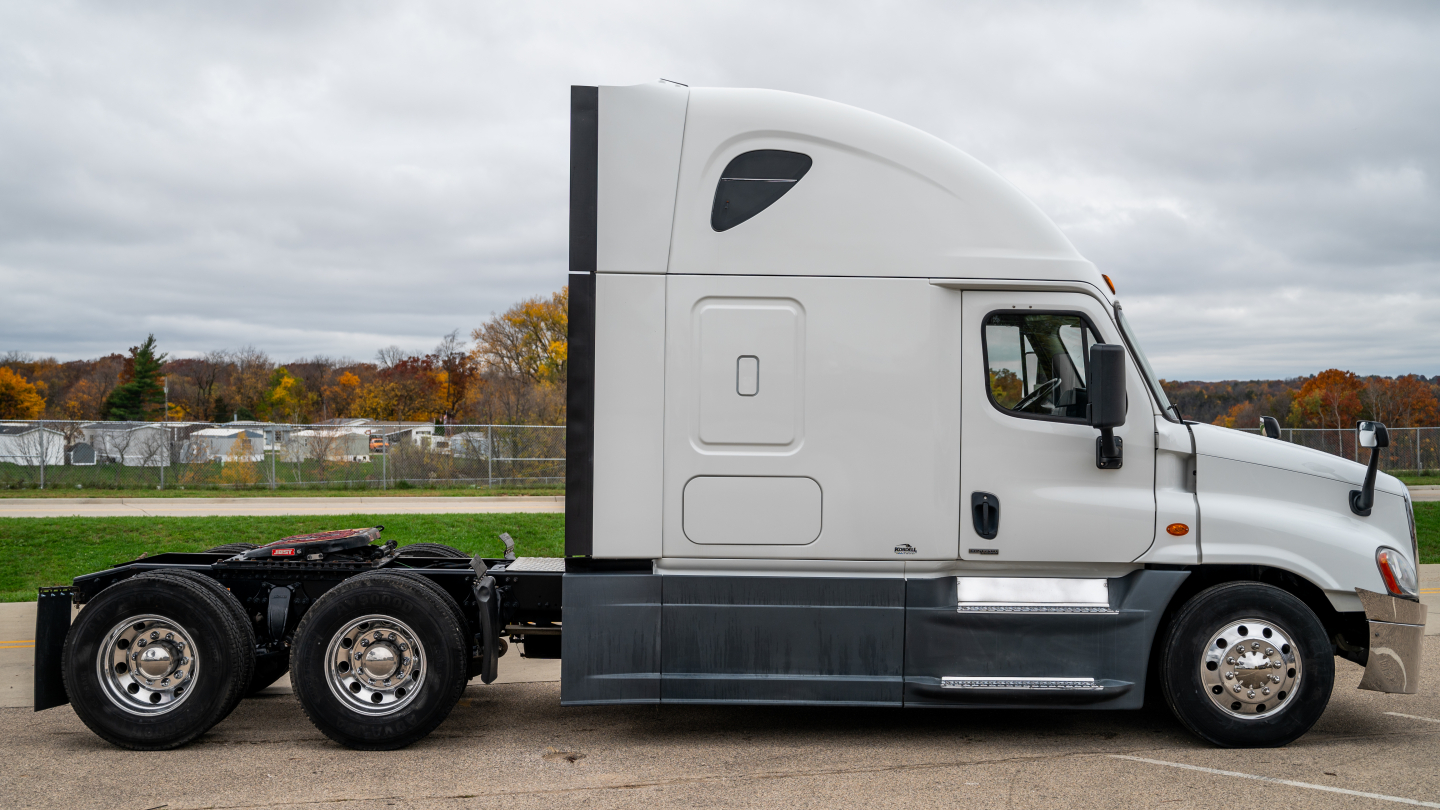 Truck side view showing sleeper cab and Freightliner badge area with white exterior and dual rear axles.