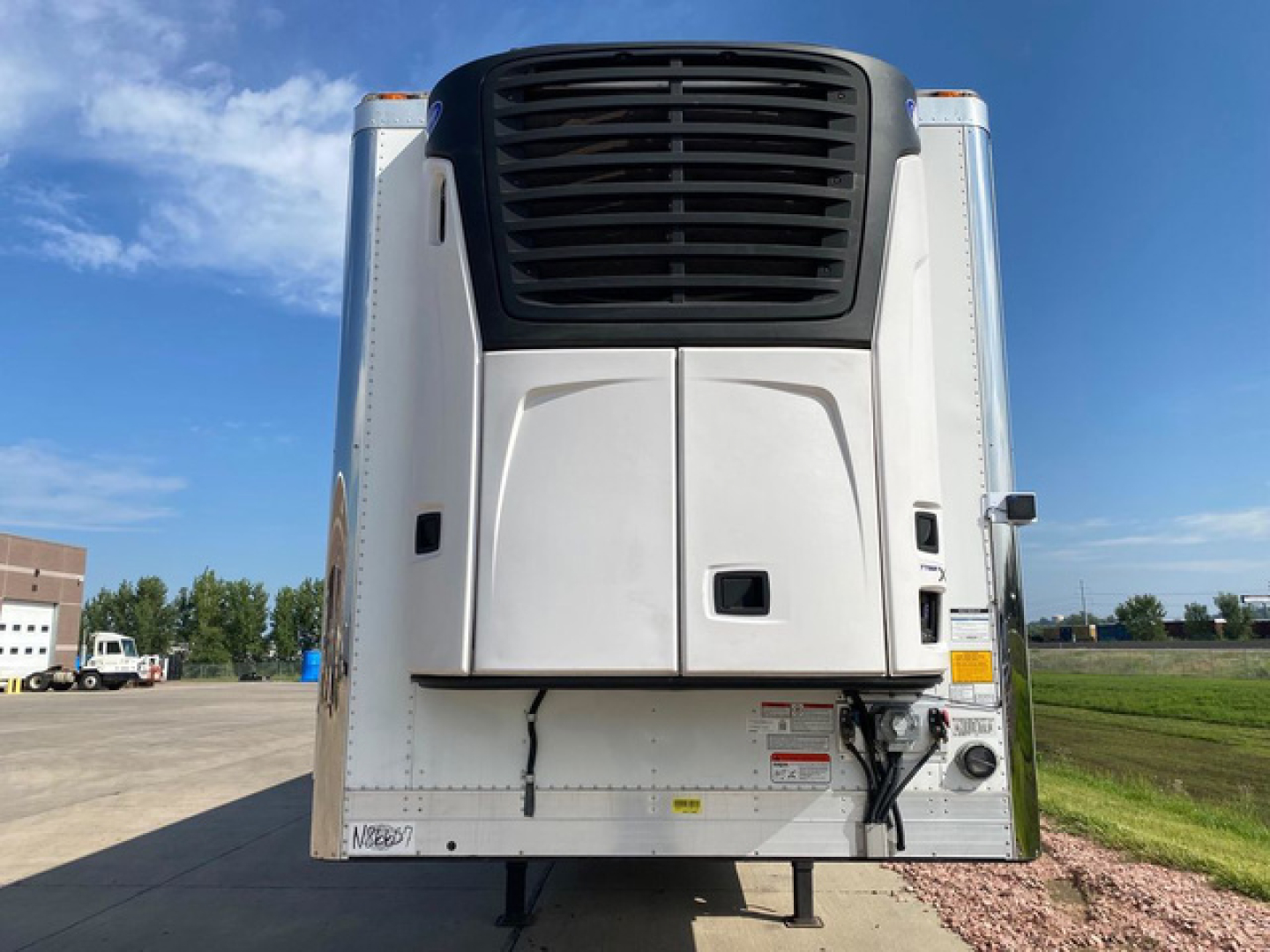 Reefer trailer rear view showing large black cooling unit and white body panels with hitch and support legs.