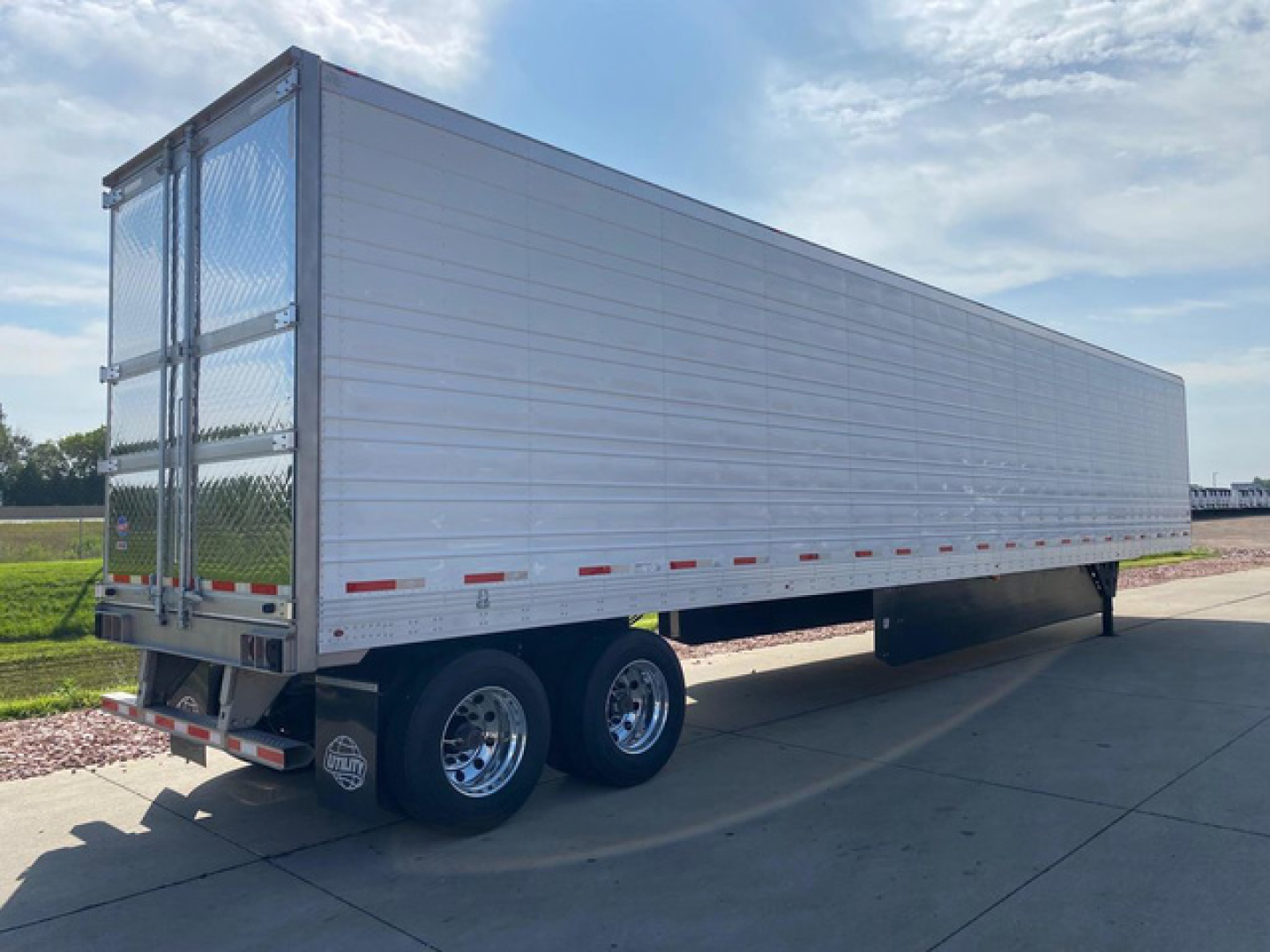 Utility reefer trailer side and rear showing aluminum exterior, tandem axles, and rear double doors with chain latching.