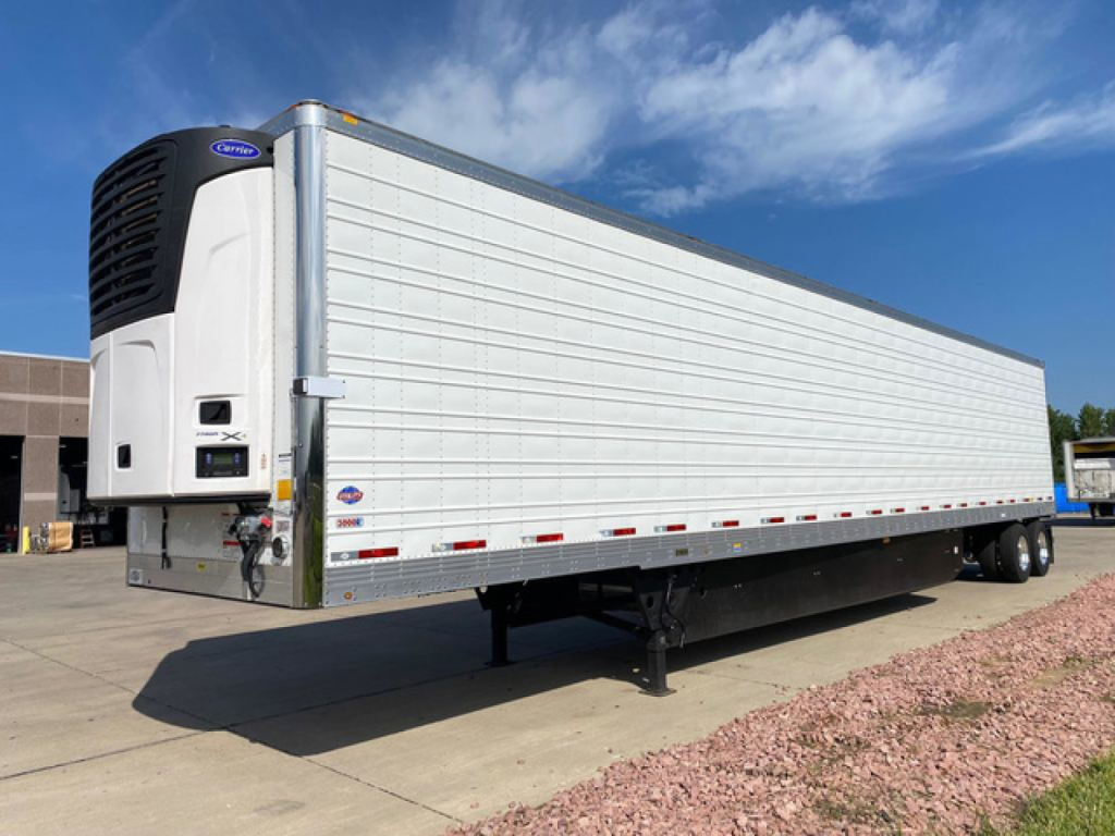 Trailer side view of a 2027 utility refrigerated trailer with a front-mounted Carrier refrigeration unit, white aluminum panels, dual rear axles, and landing gear visible.