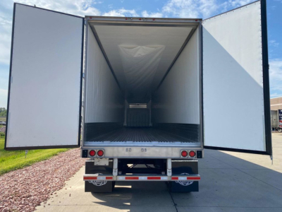 Refrigerated trailer interior with open double rear doors showing empty cargo area and floor mats.