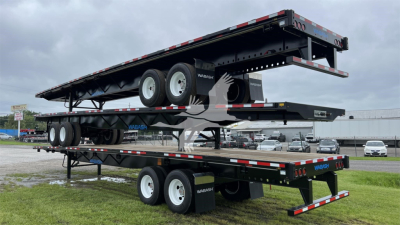 Wabash air slider flatbed trailer with tandem axles and loading ramp, stacked on a second trailer at a dealership lot.
