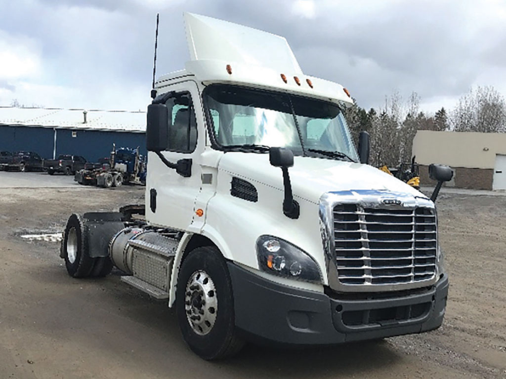 Freightliner Cascadia sleeper cab front-left view showing chrome grille, large headlights, white cab, black bumper, dual fuel tanks, and chassis without trailer.
