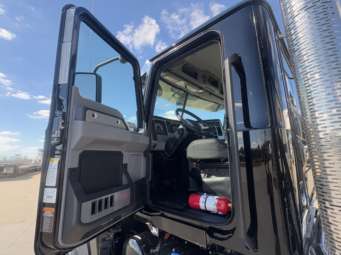 Truck cab interior view of a 2026 Mack PI64T conventional daycab with door open showing steering wheel and dashboard.
