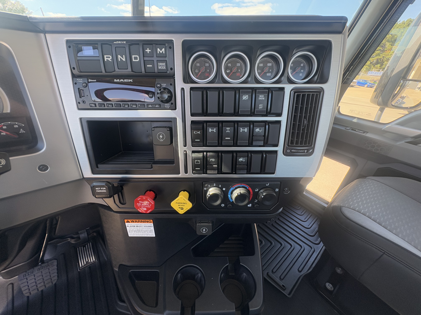 Mack PI64T dash cluster and center console showing gauges, switches, and climate controls.