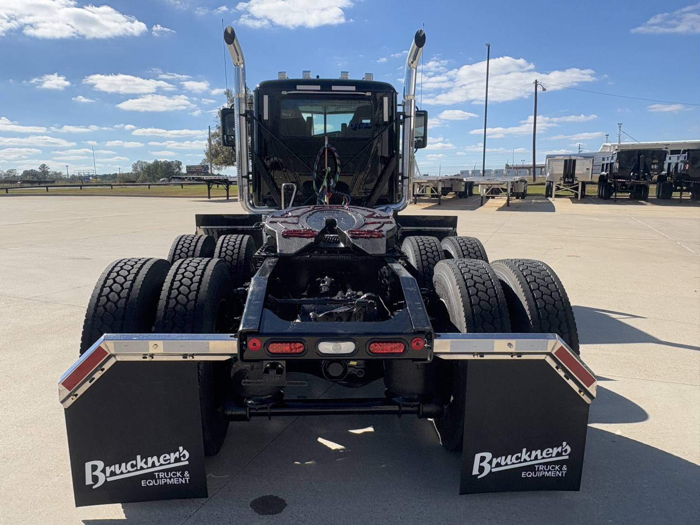 Truck rear view in a lot showing dual rear axles, mud flaps with Brückner's Truck & Equipment logo, and rear underride bumper.