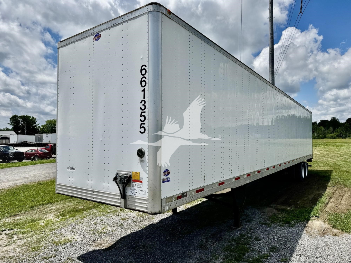 Utility dry van trailer with white exterior showing VIN and stock numbers on rear, side silhouette graphic of a bird in flight, registration stickers and rear bumper.