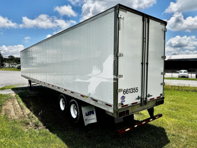 Trailer side and rear showing a silver 2016 utility dry van with dual rear doors, white vendor numbers, and black bumper; visible wheels and mid-ship reflection.