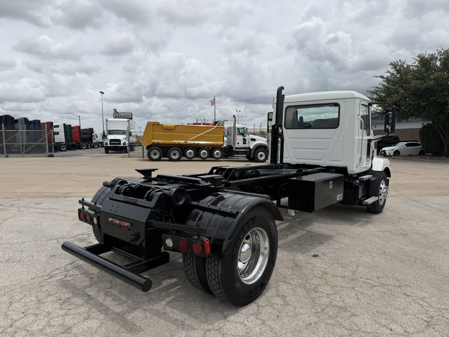 Truck chassis with cab in white, rear view showing fifth wheel and dual rear wheels, hooklift configuration on a Mack MD6 used truck.