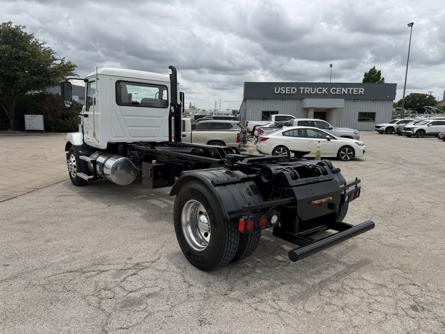 Truck chassis with cab in front, hooklift setup, rear view showing fifth wheel and rear bumper, Mack MD6 used truck at dealership lot.
