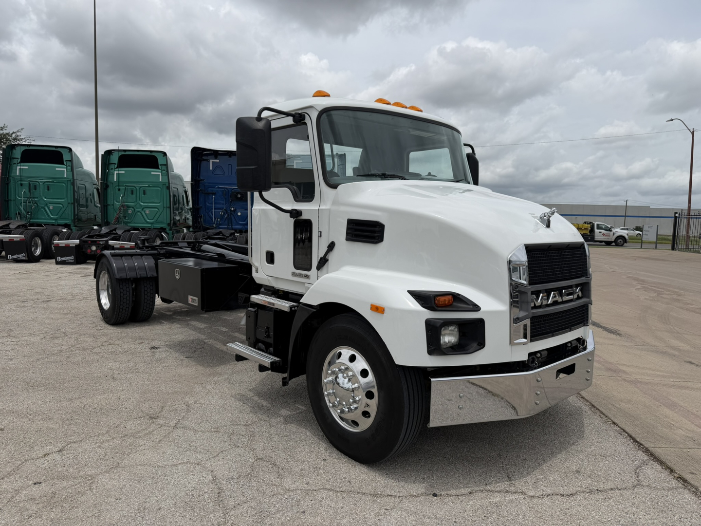 Mack MD6 hooklift truck front quarter view showing white cab, a black grille, chrome bumper, and side mirrors; appears used in a dealership lot.