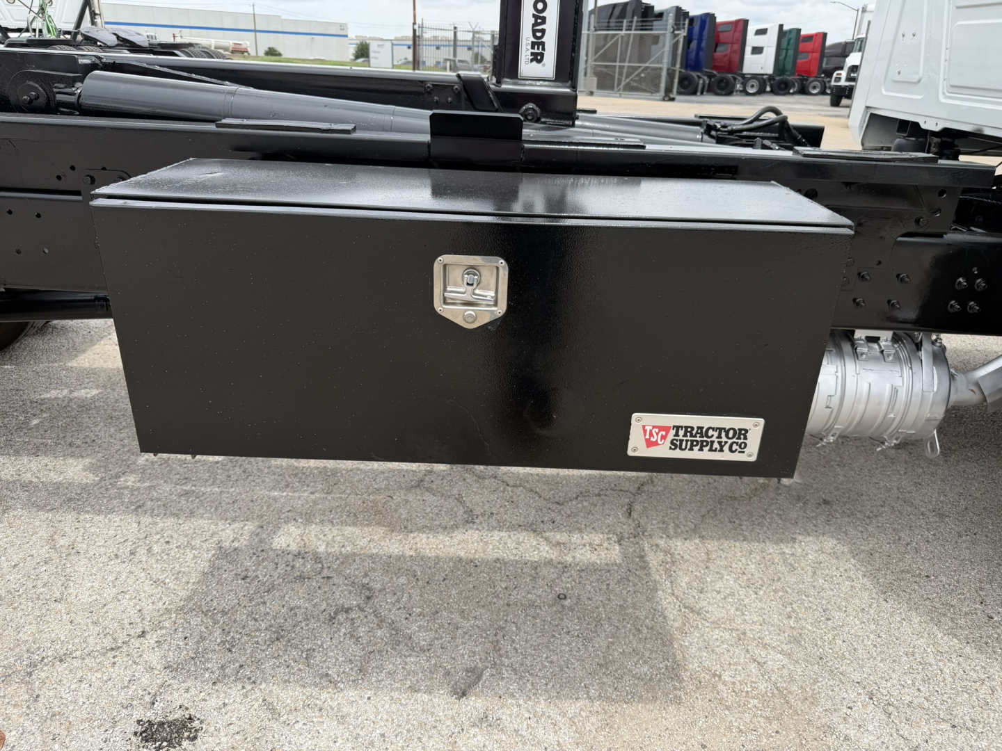 Mack MD6 truck chassis side with black rectangular tool/storage box under bed showing latch and Tractor Supply Co. logo plate.