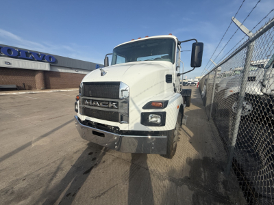2024 Mack MD6 hooklift truck front view with bold grille and headlights. Visible text includes MACK on grille and Volvo building in background.