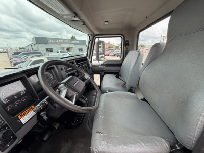 Cab interior of a 2024 Mack MD6 hooklift truck showing steering wheel, instrument cluster, driver and passenger seats with wear on seat edge.