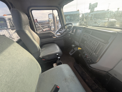 Cab interior of a Mack MD6 truck showing steering wheel, dashboard, and two seats from passenger side; visible control panel and gear shifter.