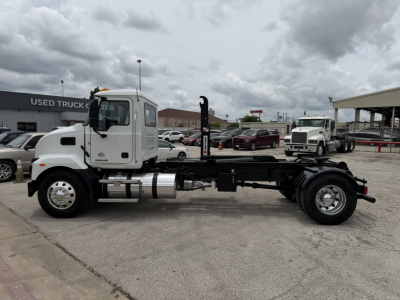 White Mack MD6 hooklift truck chassis side view showing fuel tank, exhaust, and hydraulic components.