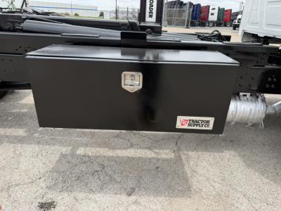 Mack MD6 truck chassis side with black rectangular tool/storage box under bed showing latch and Tractor Supply Co. logo plate.