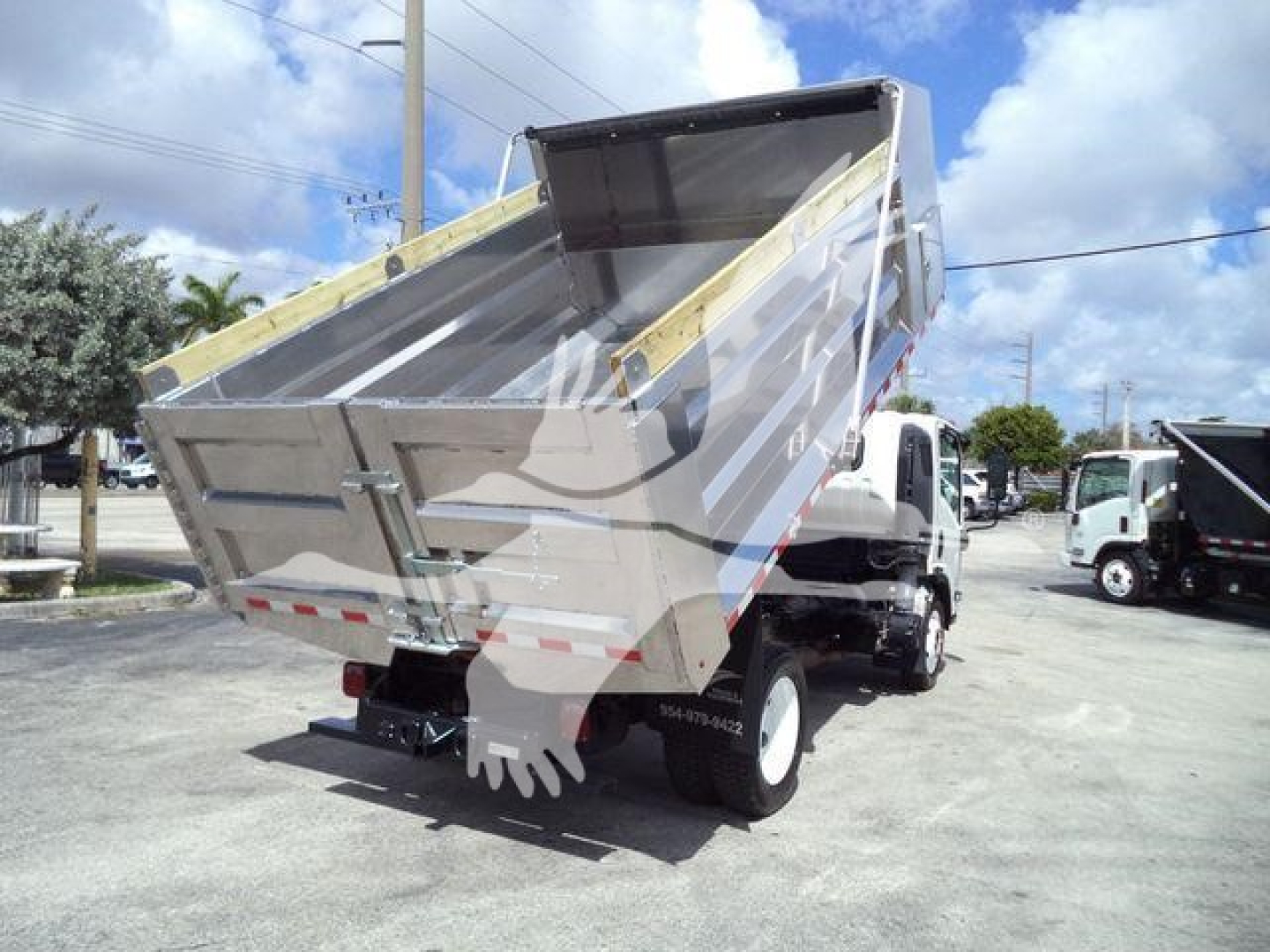 Isuzu NPR-HD dump truck bed raised showing side and rear with metal dump bed, hydraulic lift, and tailgate latches.