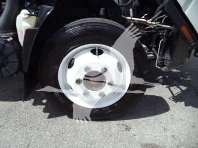 Isuzu NPR HD truck front wheel showing white steel rim and tire, part of dump truck chassis, visible hydraulic lines and suspension components.