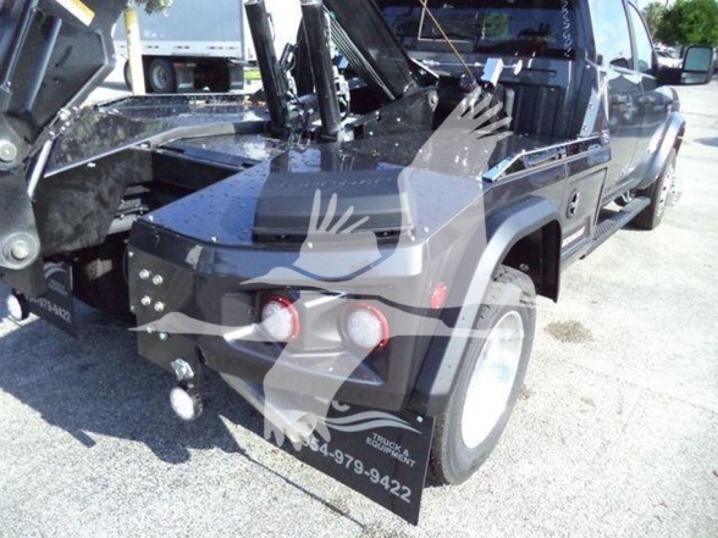 Ram pickup bed showing winch system and front bumper with two round headlights; visible text on bumper area includes phone number and branding, with open hood and equipment in bed.