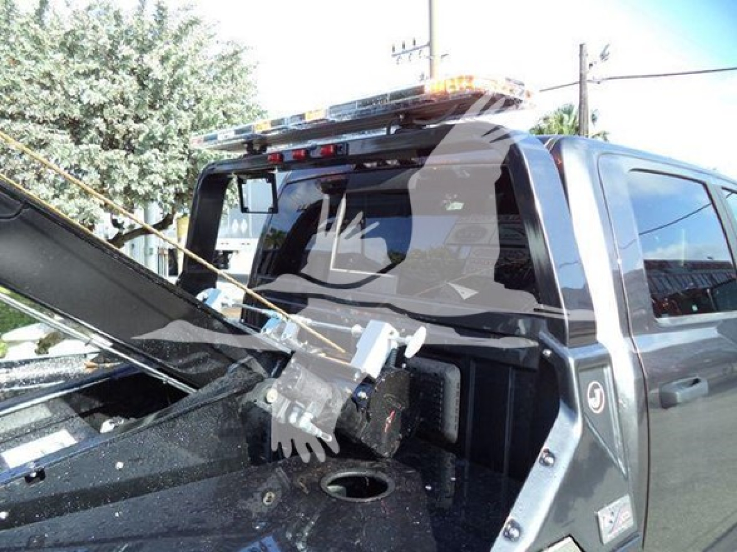Ram truck rear cab area with a winch setup in the bed, visible windshield, rear window, and a roof beacon light; no legible model text.
