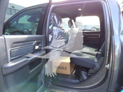 Ram pickup truck interior shown with front passenger door open, cardboard box labeled FRAGILE on seat, vinyl wrap covering seats.