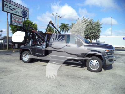 Ram pickup truck in showroom/lot with winch equipment attached at rear, side view showing crew cab, chrome wheels, and hydraulic crane assembly.