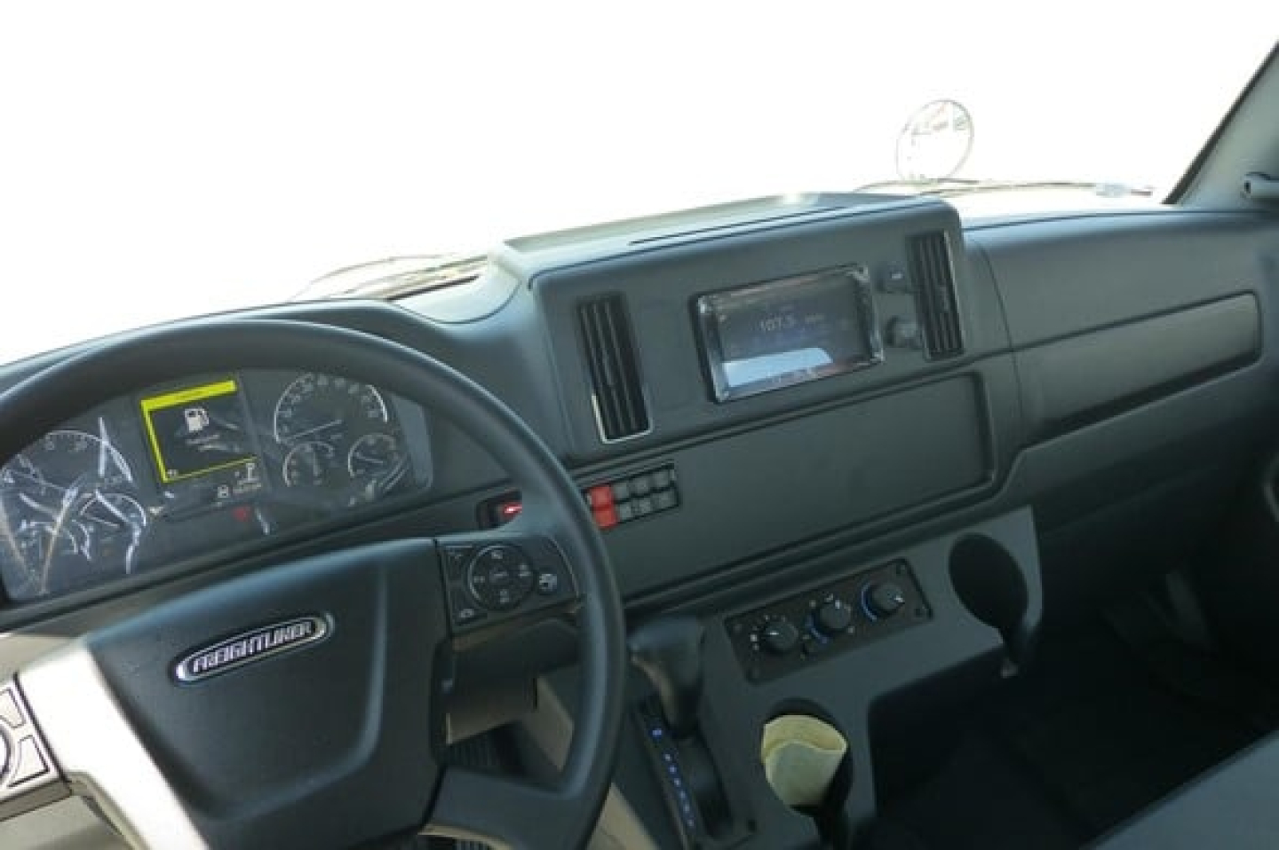 Freightliner Business Class M2 106 Plus cab interior showing steering wheel, dashboard with gauges, center console, and touchscreen display.