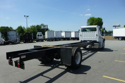 Freightliner Business Class M2 106 Plus cab and chassis frame seen from rear-left side, with white cab and long black chassis frame; trailer connections and rear lights visible