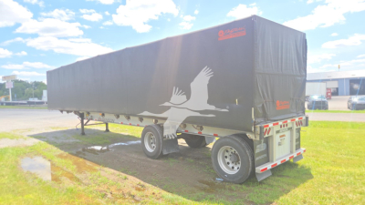Conestoga style Benson flatbed trailer with a black tarp cover and white bird graphic, viewed from rear-left side.