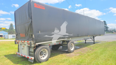 Trailer showing a curtain-side Benson flatbed tractor trailer with a gray tarp, white crane-like bird logo on the side, dual rear wheels, and red-and-white reflective tape.
