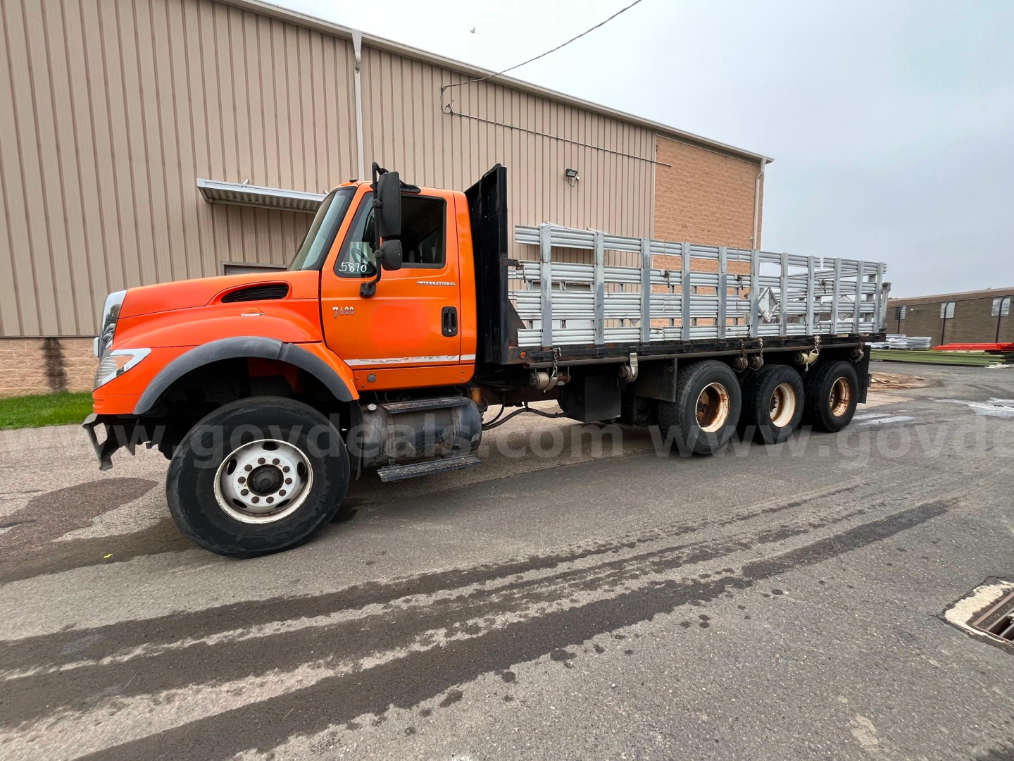 Orange 2004 International 7600 flatbed dump truck side view showing long dual rear axles and aluminum stake bed.