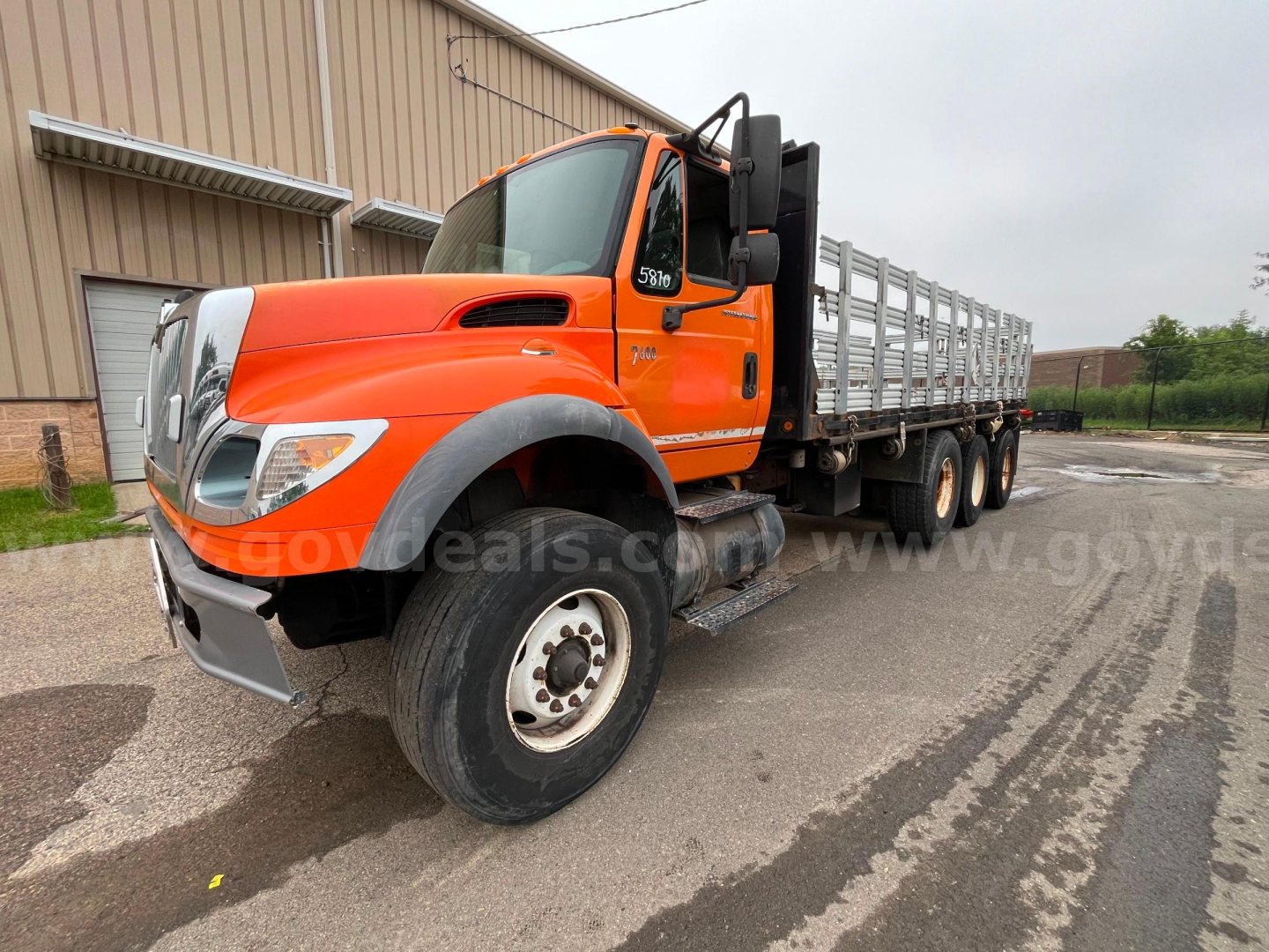 2004 International 7600 flatbed dump truck with orange cab and black chassis, showing front wheel, side cab details, flatbed with metal rails, and a stored crane behind cab.