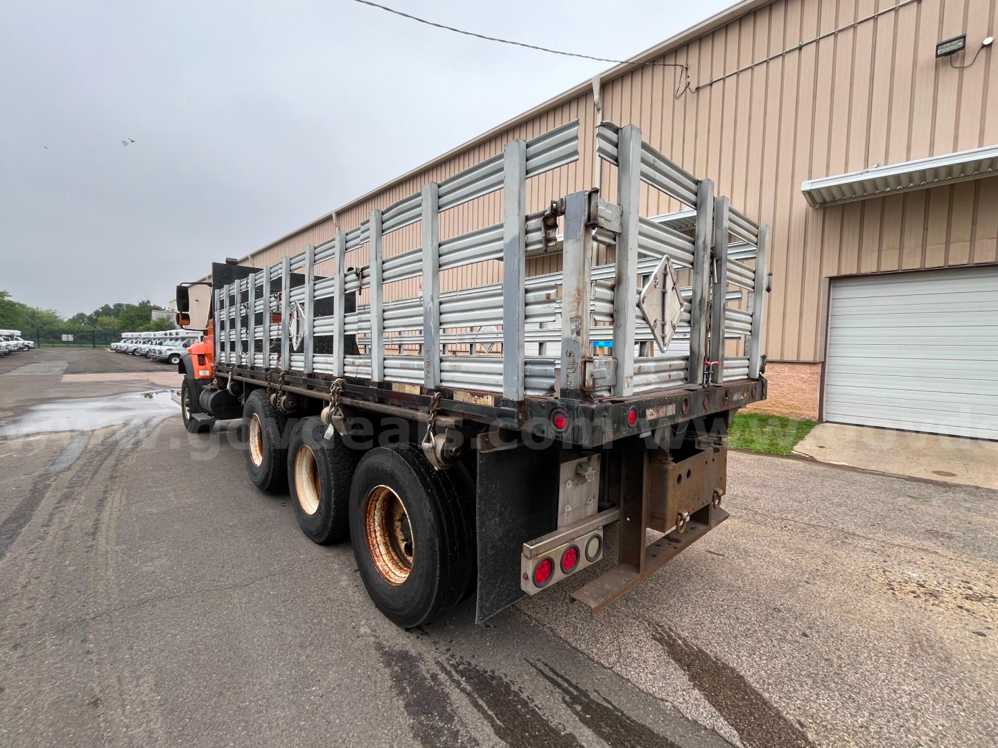 Used 2004 International 7600 flatbed dump truck rear view showing triple rear axles and metal stake-sided bed.