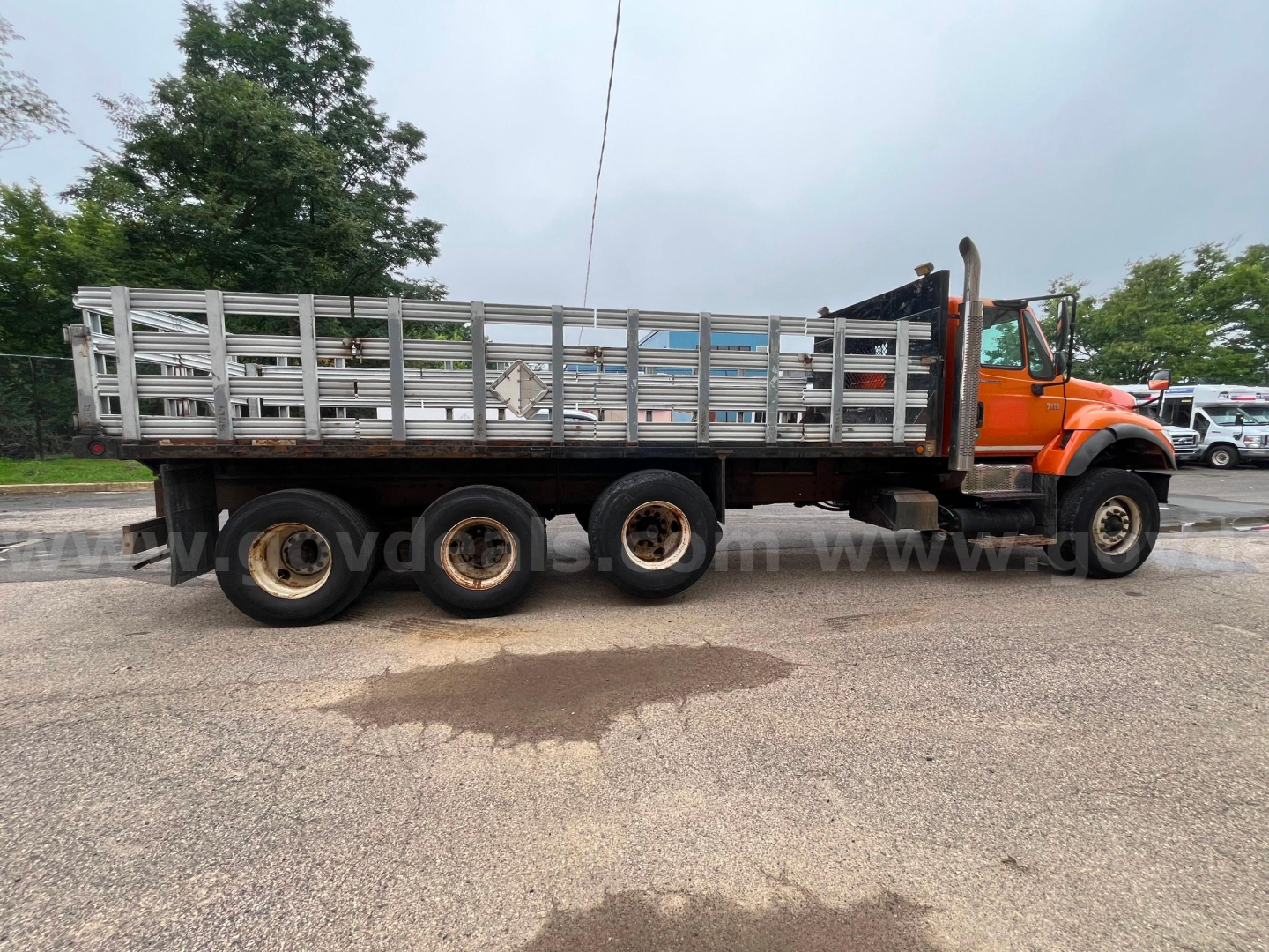2004 International 7600 flatbed dump truck side profile showing long stake body and orange cab.