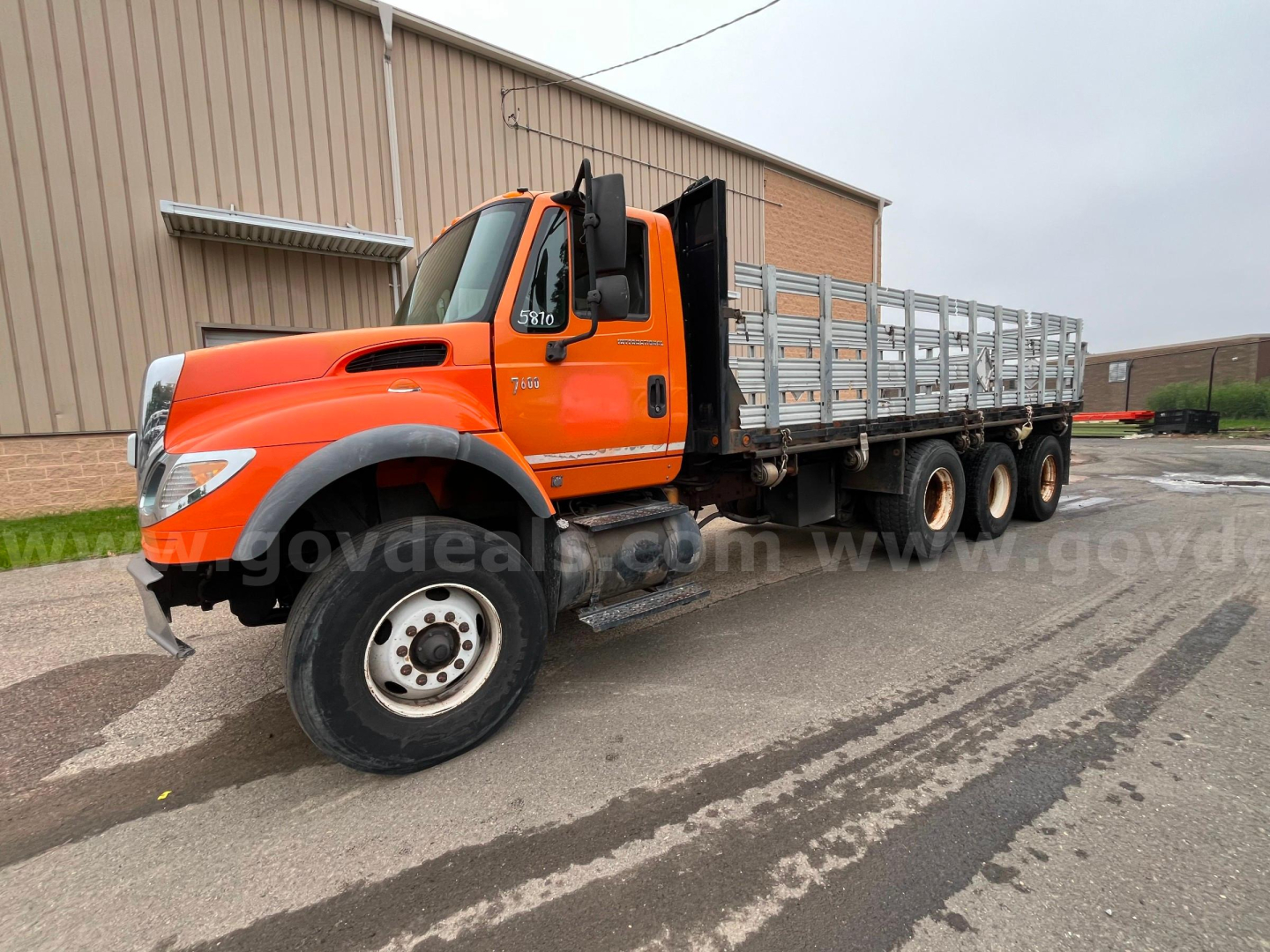 International 7600 flatbed dump truck in-service showing orange cab and long aluminum-sided flatbed with triple rear axle configuration.