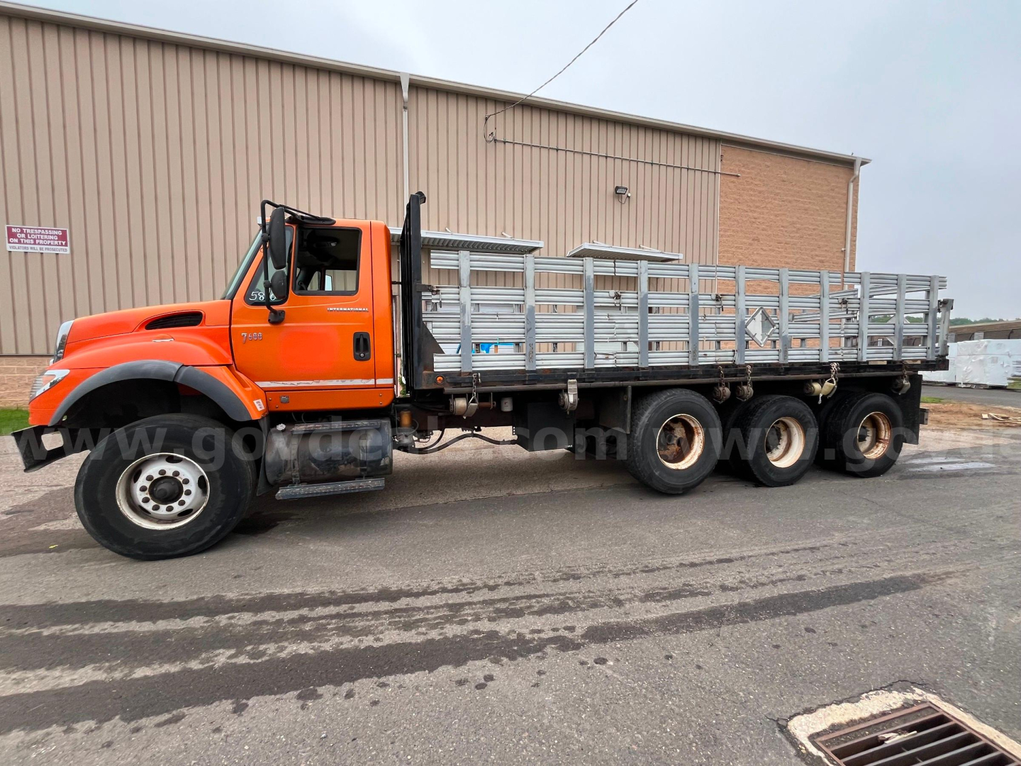 International 7600 flatbed dump truck side view showing orange cab and long dual rear axle with metal sided flatbed.
