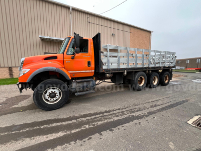 Orange 2004 International 7600 flatbed dump truck side view showing long dual rear axles and aluminum stake bed.
