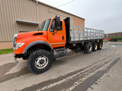 International 7600 flatbed dump truck in-service showing orange cab and long aluminum-sided flatbed with triple rear axle configuration.