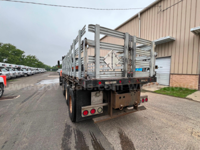 Truck bed of a 2004 International 7600 flatbed dump with dual rear axles and metal side rails, rear view showing tailgate and bumper.