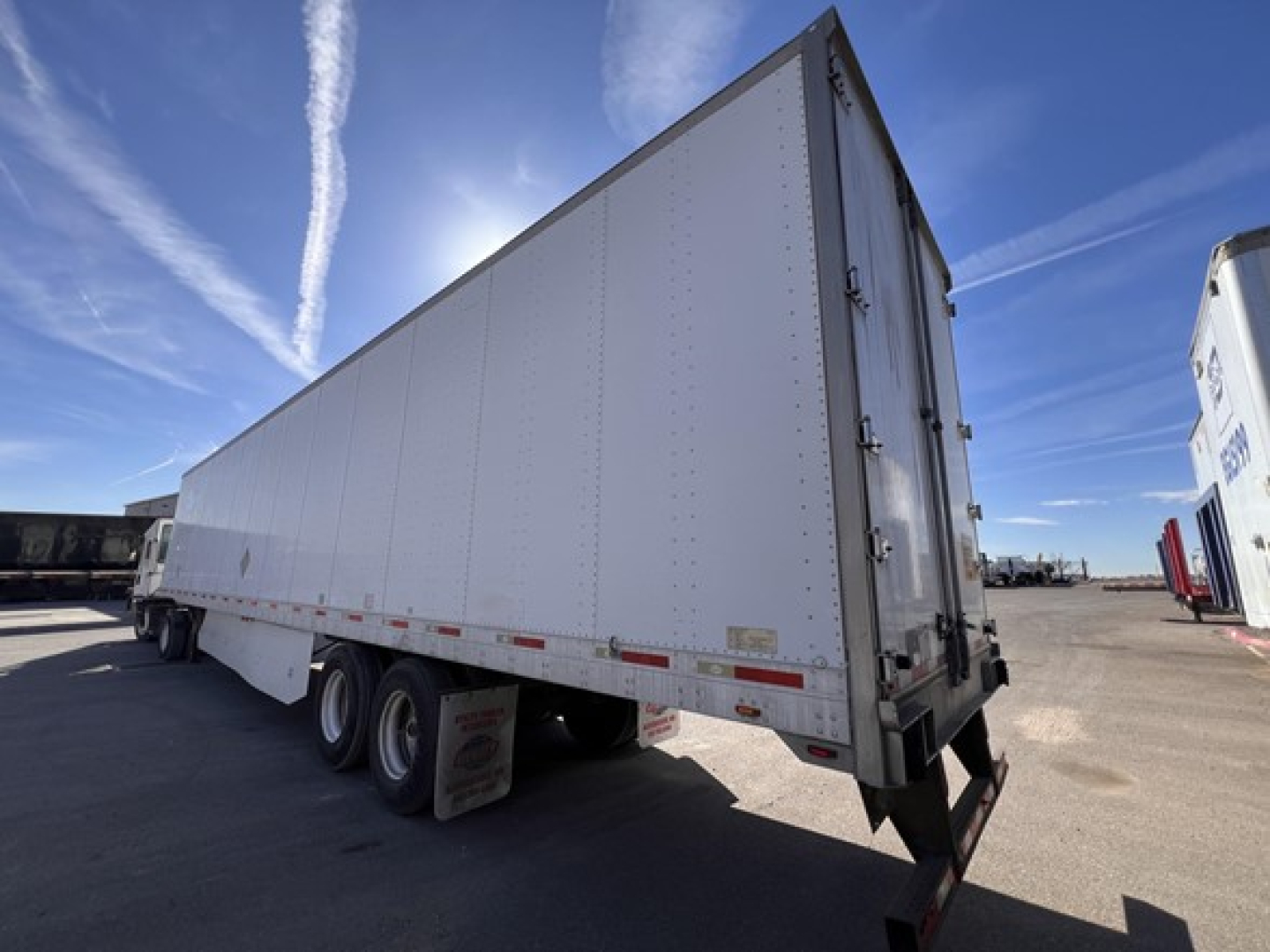Utility dry van trailer with rear swing doors, three-axle undercarriage, side reflective tape and DOT bumper.