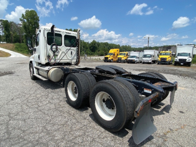 Truck chassis and cab of a 2020 Freightliner Cascadia125 tractor, rear dual axles visible with white rims, fifth-wheel and mud flaps; yard with other trucks in background.
