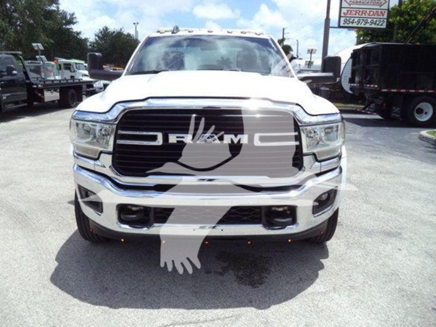 Front view of a white 2021 RAM Ram truck showing chrome grille with RAM lettering, headlights, and bumper; dealership lot in background.