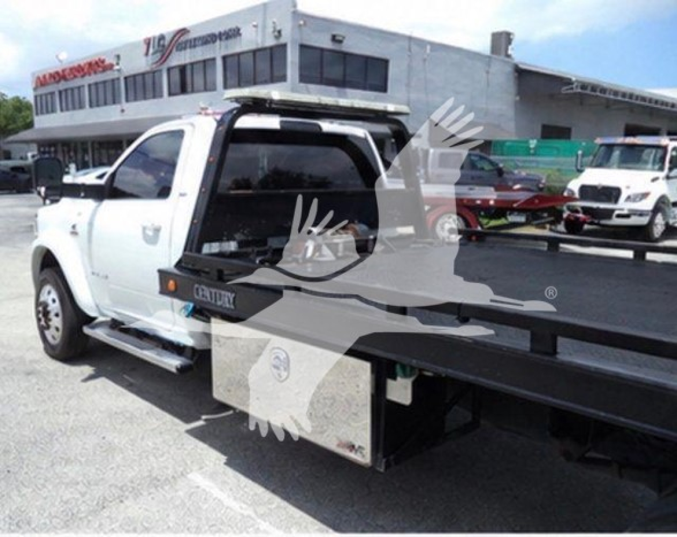 Ram pickup truck with rollback tow bed, side view showing utility toolbox and open rear bed in a dealership lot.